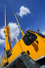 Mobile construction cranes with telescopic arms mounted on trucks with yellow bodyworks in sunny day with white clouds and deep blue sky on background, heavy industry 