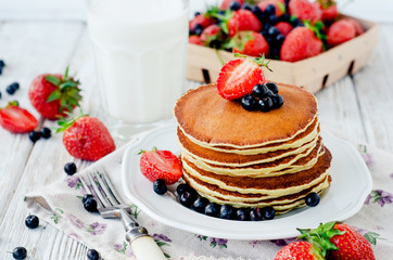 
easy hearty and healthy breakfast , American pancakes with berries , blueberries and strawberries with milk on a wooden background