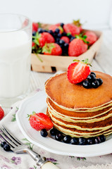 
easy hearty and healthy breakfast , American pancakes with berries , blueberries and strawberries with milk on a wooden background