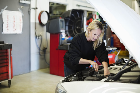 Mid adult female mechanic repairing car engine at auto repair shop
