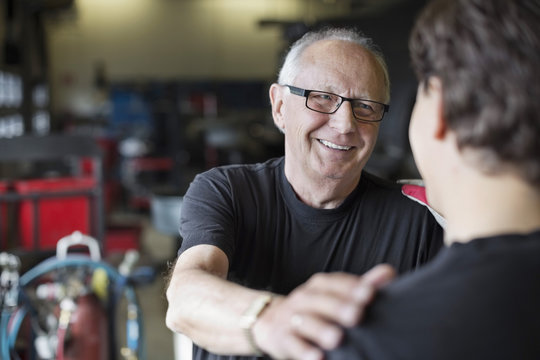 Happy senior male mechanic looking at coworker in auto repair shop