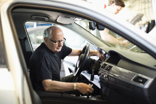 Senior male mechanic examining gearshift while sitting on driver's seat in car