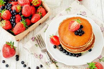 
easy hearty and healthy breakfast , American pancakes with berries , blueberries and strawberries with milk on a wooden background