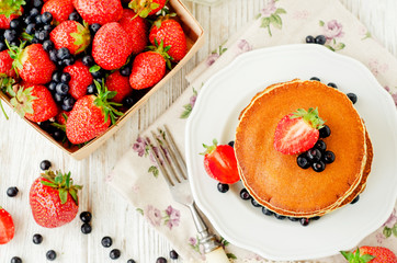 
easy hearty and healthy breakfast , American pancakes with berries , blueberries and strawberries with milk on a wooden background