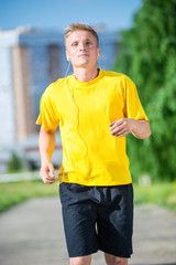Running man jogging in city street park at beautiful summer day. Sport fitness model caucasian ethnicity training outdoor. Jogger listening training music on smartphone 