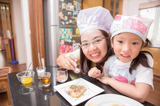 Asian mother and daughter enjoy making pancake in kitchen