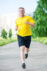 Running man jogging in city street park at beautiful summer day. Sport fitness model caucasian ethnicity training outdoor.