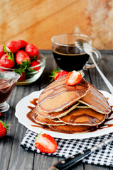 
easy hearty and healthy breakfast , American pancakes with strawberries and chocolate with coffee on a wooden background