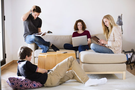 Young friends with magazine, laptop and digital tablet in living room