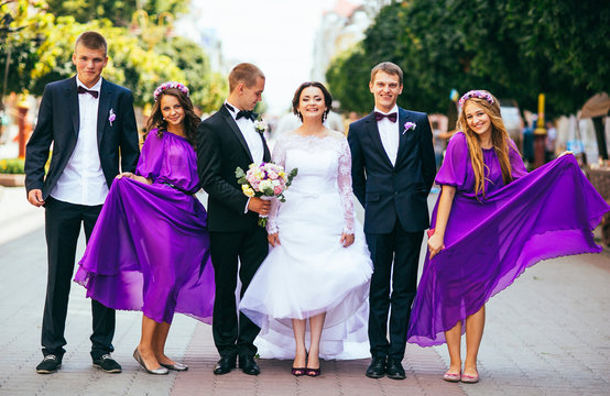 Newlywed couple, bridesmaids & groomsmen having fun outdoors. Bridesmaids in purple (violet) dress. Walking in the city. 
