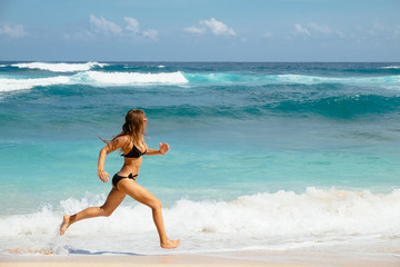 Woman running through sea water on a beach in Bali. Female runner jogging during outdoor workout on beach.
