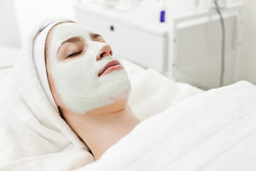 Young woman relaxing on massage table with facial mask at beauty spa