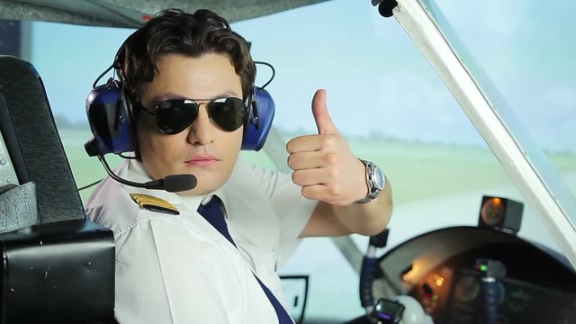 Serious pilot in sunglasses making thumbs up hand sign, plane ready for takeoff