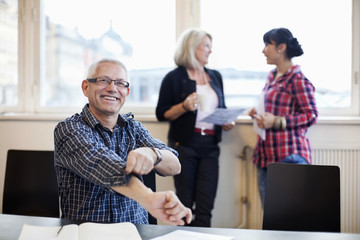 Mature businessman rolling sleeves up with colleagues discussing in background