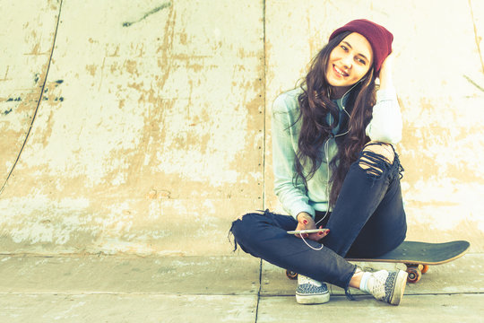 Hipster skateboarder girl with skateboard outdoor sitting at skatepark