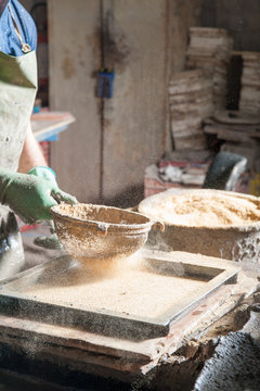 Red brick artisan strewing sawdust at the base of a mould before putting the clay to model
