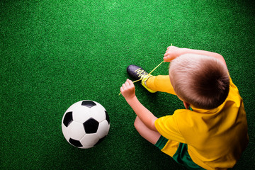 Unrecognizable little football player against green grass, studi