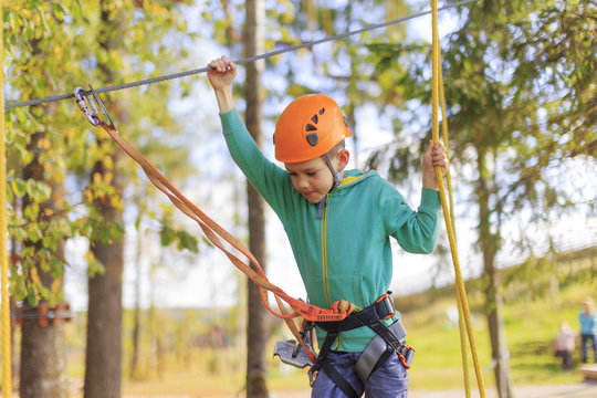 boy enjoys climbing in the ropes course adventure. smiling child engaged climbing high wire park