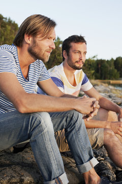 Two male friends contemplating while sitting on rock