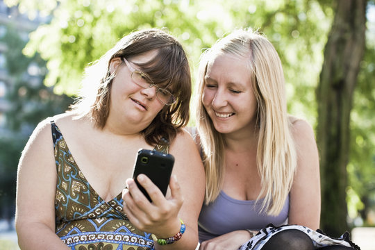 Young woman with down syndrome her personal assistant looking at phone together