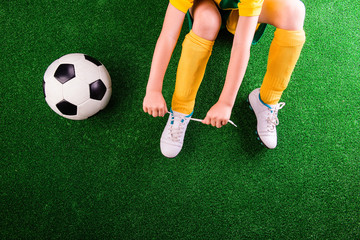 Unrecognizable little football player against green grass, studi