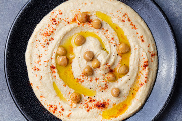 Hummus, chickpea dip, with spices and pita, flat bread in a black plate on grey stone background