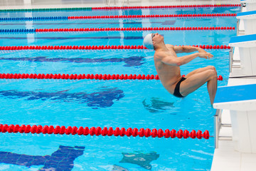 Young muscular swimmer jumping from starting block in a swimming pool