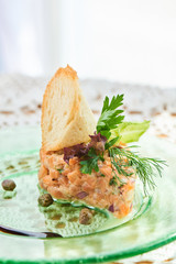 A dish of salmon tartare, red and green onions, lemon zest and olive oil served on a plate