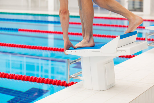 Young muscular swimmer in low position on starting block in a swimming pool