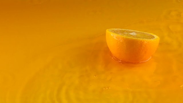 Half of ripe orange hits orange juice surface and rebounces. Slow motion video