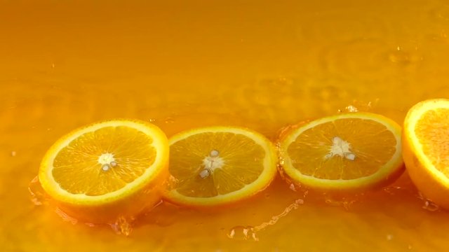 Cut ripe orange hits orange juice surface and rebounces. Slow motion video