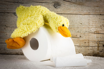Toilet paper with funny plush duck on wooden background