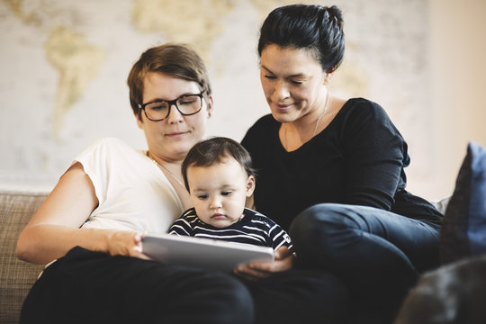 Women with toddler looking in digital tablet while sitting at home