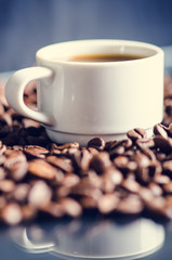 Coffee beans and cup on a black background. Raw coffee beans. Grained product. Hot drink. Close up. Harvesting. Natural background. Energy. Reflection in a glass 