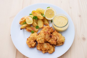 Cod fish in batter or cod fritters served with baked potatoes with parsley leaves and home made mayonnaise sauce and half of lemon served on the simple white plate. Light dish for lunch or diner. 