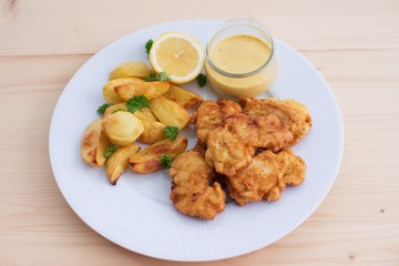 Cod fish in batter or cod fritters served with baked potatoes with parsley leaves and home made mayonnaise sauce and half of lemon served on the simple white plate. Light dish for lunch or diner. 