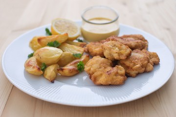 Cod fish in batter or cod fritters served with baked potatoes with parsley leaves and home made mayonnaise sauce and half of lemon served on the simple white plate. Light dish for lunch or diner. 