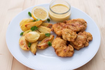 Cod fish in batter or cod fritters served with baked potatoes with parsley leaves and home made mayonnaise sauce and half of lemon served on the simple white plate. Light dish for lunch or diner. 