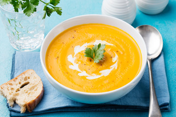 Pumpkin and carrot soup with cream and parsley on blue stone background