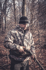 Fototapeta premium Hunter man loading shotgun during hunting in autumn forest with dry trees and leaves