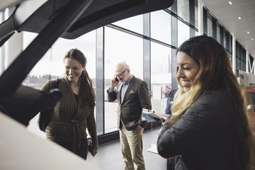 Happy friends looking at car while senior man using phone in showroom