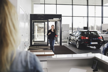 Smiling woman walking towards sales clerk at car showroom