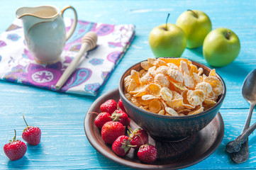 Cornflakes in a bowl with milk and fruits on the table