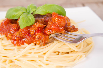 Spaghetti bolognese decorated with basil being eaten with a fork