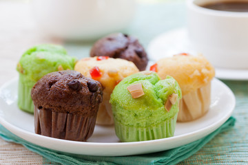 Assortment of muffins vanilla, chocolate, pandan on a white plate. Outdoor tropical background