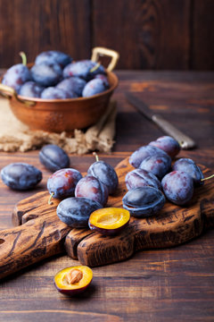 Fresh organic plums in copper bowl and on rustic wooden cutting board