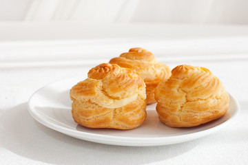 Profiteroles, choux with a custard cream, creme anglaise, whipped cream, dessert on a white plate