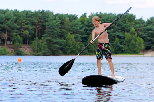 Adventurous boy learning to paddle on stand up board. Happy child, teenage schoolboy, having fun enjoying adventurous experience on the river on a sunny day during summer holidays