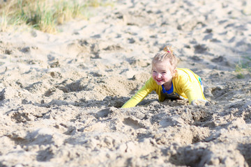 Cute active child playing on wide sandy beach jumping in dunes. Happy little girl enjoying summer holidays on a sunny day. Family with young kids on vacation at the North Sea coast.