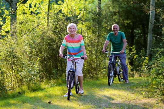 Happy healthy couple biking together in the forest. Seniors enjoying sunny day outdoors. Active retirement concept.